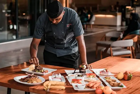 Image of a chef in a restaurant adjusitng the detials of a plating of food.