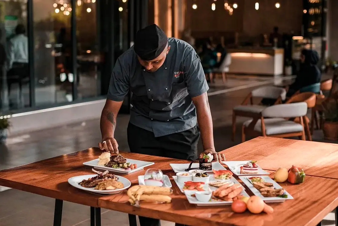 Image of a chef in a restaurant adjusitng the detials of a plating of food.