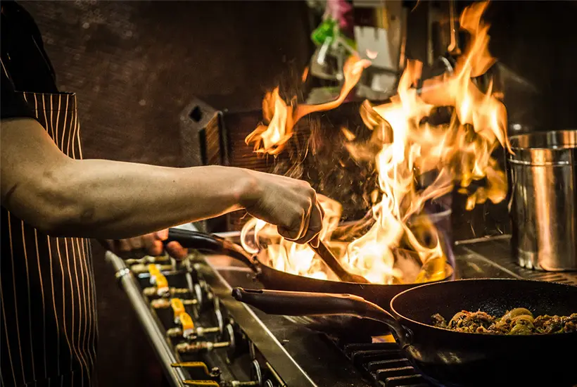 Image of a chef cooking on a stovetop with flames rising from the pan.