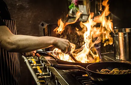 Image of a chef cooking on a stovetop with flames rising from the pan.