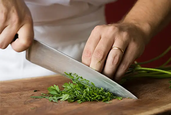 Close up image of a chef's hands chopping cilantro on a cutting board.