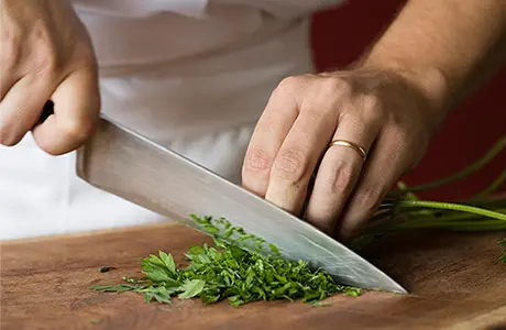 Close up image of a chef's hands chopping cilantro on a cutting board.