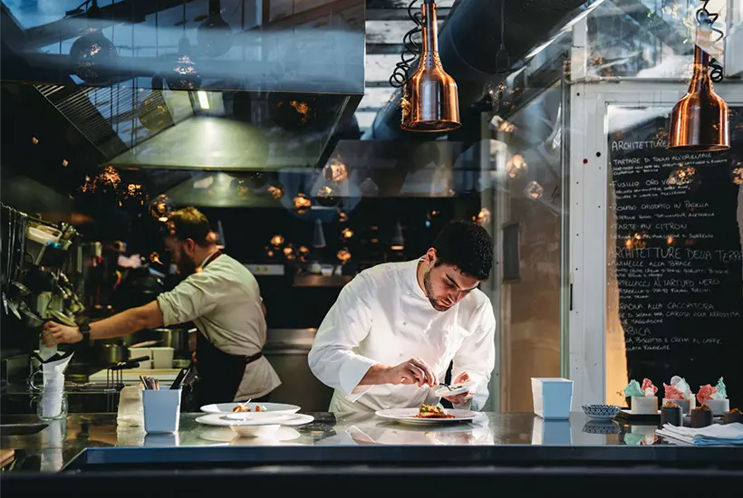 Image of a chef in a kitchen working on the details of a plating.