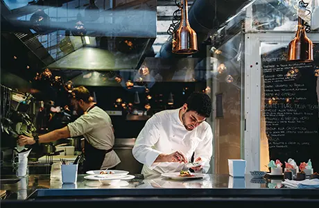 Image of a chef in a kitchen working on the details of a plating.