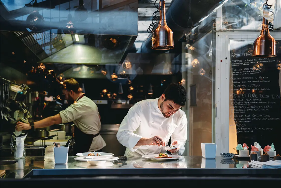 Image of a chef in a kitchen working on the details of a plating.