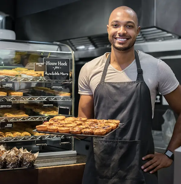 Image of a kitchen worker proudly holding a pan of fresh baked goods.