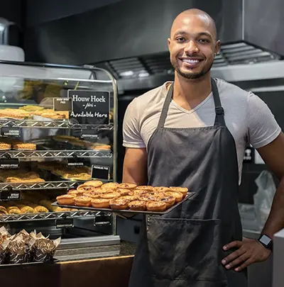 Image of a kitchen worker proudly holding a pan of fresh baked goods.
