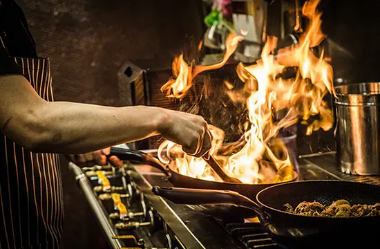 Image of a chef cooking on a stove top using a pan filled with flames.