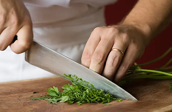 Close up image of a chef's hands as they chop cilantro on a cutting board.