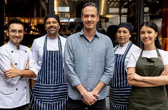 A group of kitchen workers smiling as they syand side by side.